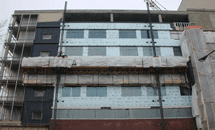 A multi-storey building undergoing exterior cladding replacement, with scaffolding and new insulation panels installed over the façade.
