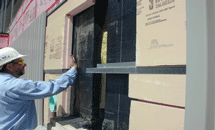 A worker installing insulation board and metal flashing as part of a glazing and curtainwall assembly.